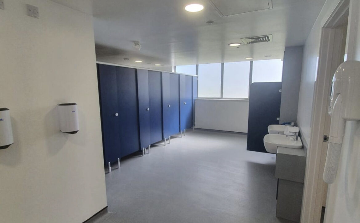 Commercial washroom with blue cubicle doors and white walls.