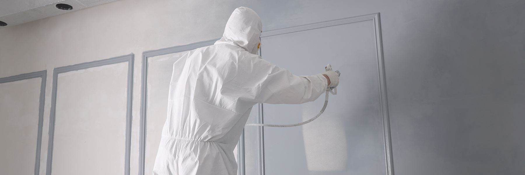Man spray painting internal wall grey.